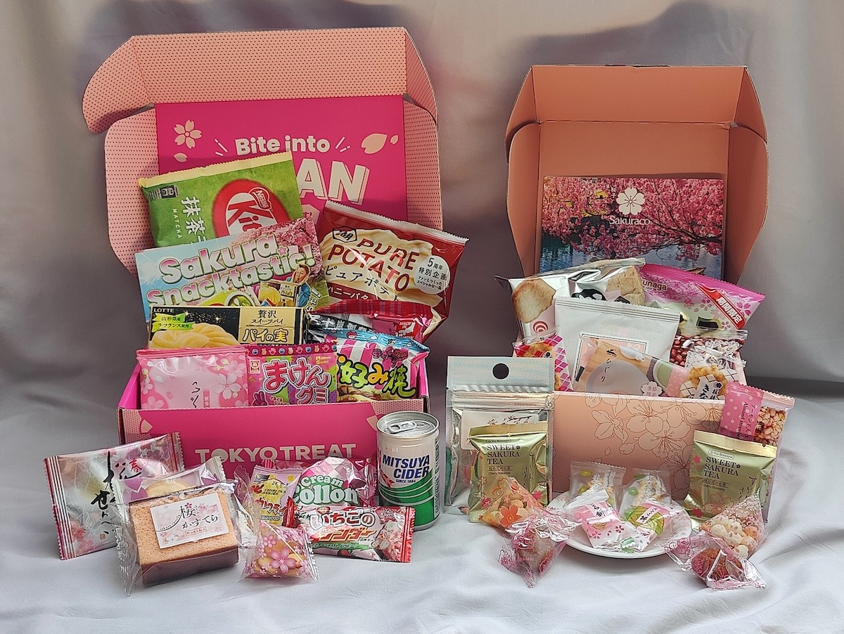 A photo of a Tokyo Treat box and Sakuraco box opened, side by side to show all of their contents. The Tokyo Treat box is slightly larger, and contains candies, baked goods, ramen, seasonal matcha latte KitKit, Japanese soda Mitsuya Cider, and ramen. The Sakuraco box contains traditional snacks, rice crackers, a ceramic dish, and sakura tea pairing