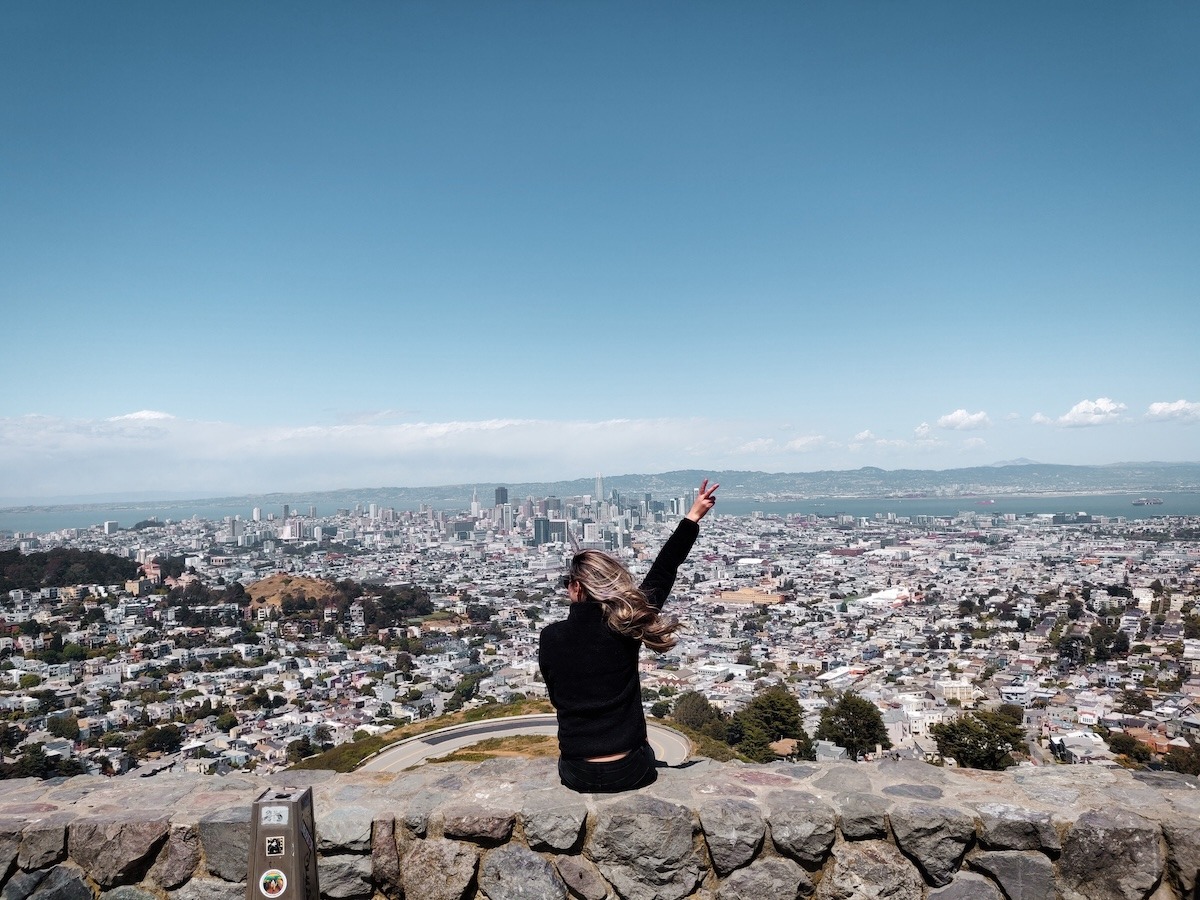 A woman sits on a ledge looking out at the San Francisco skyline