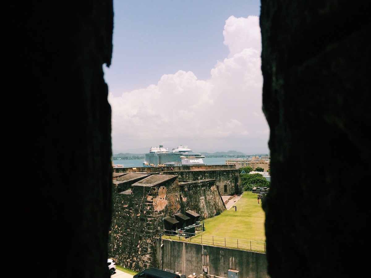 A cruise ship is docked in the background, seen from Castillo de San Cristobal with remnants of the fortress in the foreground