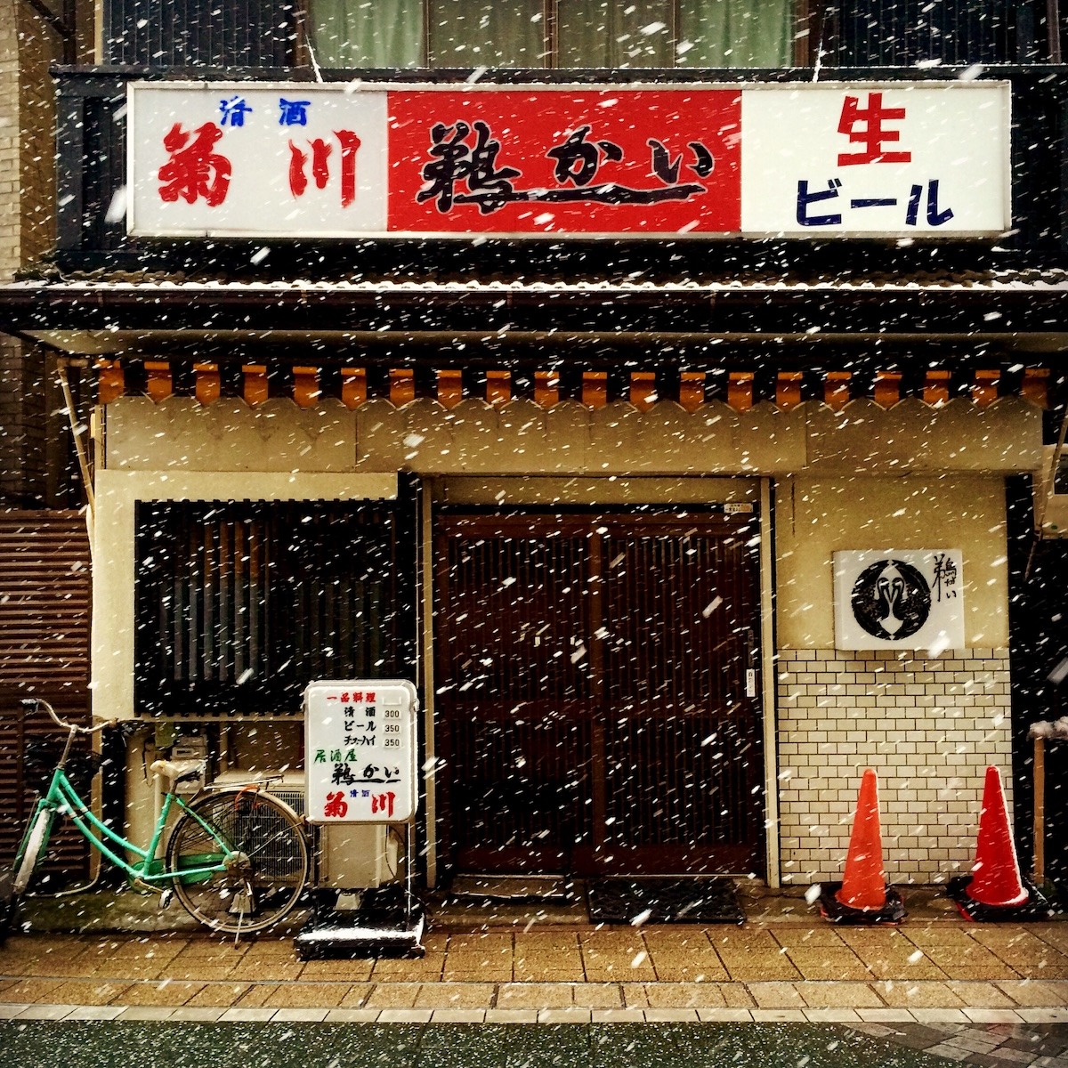 A Japanese bar with a green bicycle with snow falling