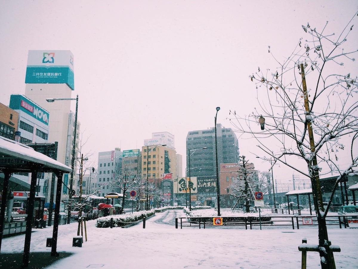 A winter scene in Japan with tall buildings surrounded by snow on the ground