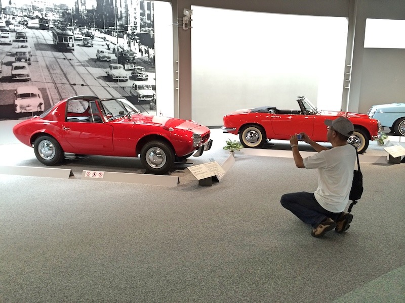 A man takes a picture of a red classic Toyota car