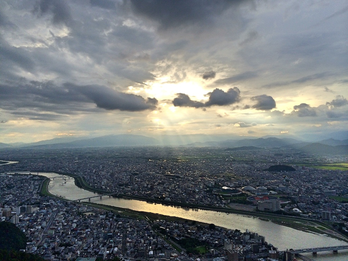 The sun breaking through clouds above a city with a river cutting through