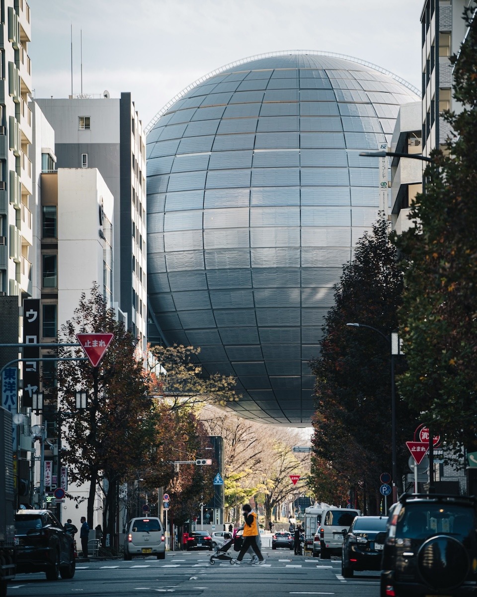 A large silver sphere (part of the Nagoya City Science Museum) appears to float above a street in Nagoya, Japan