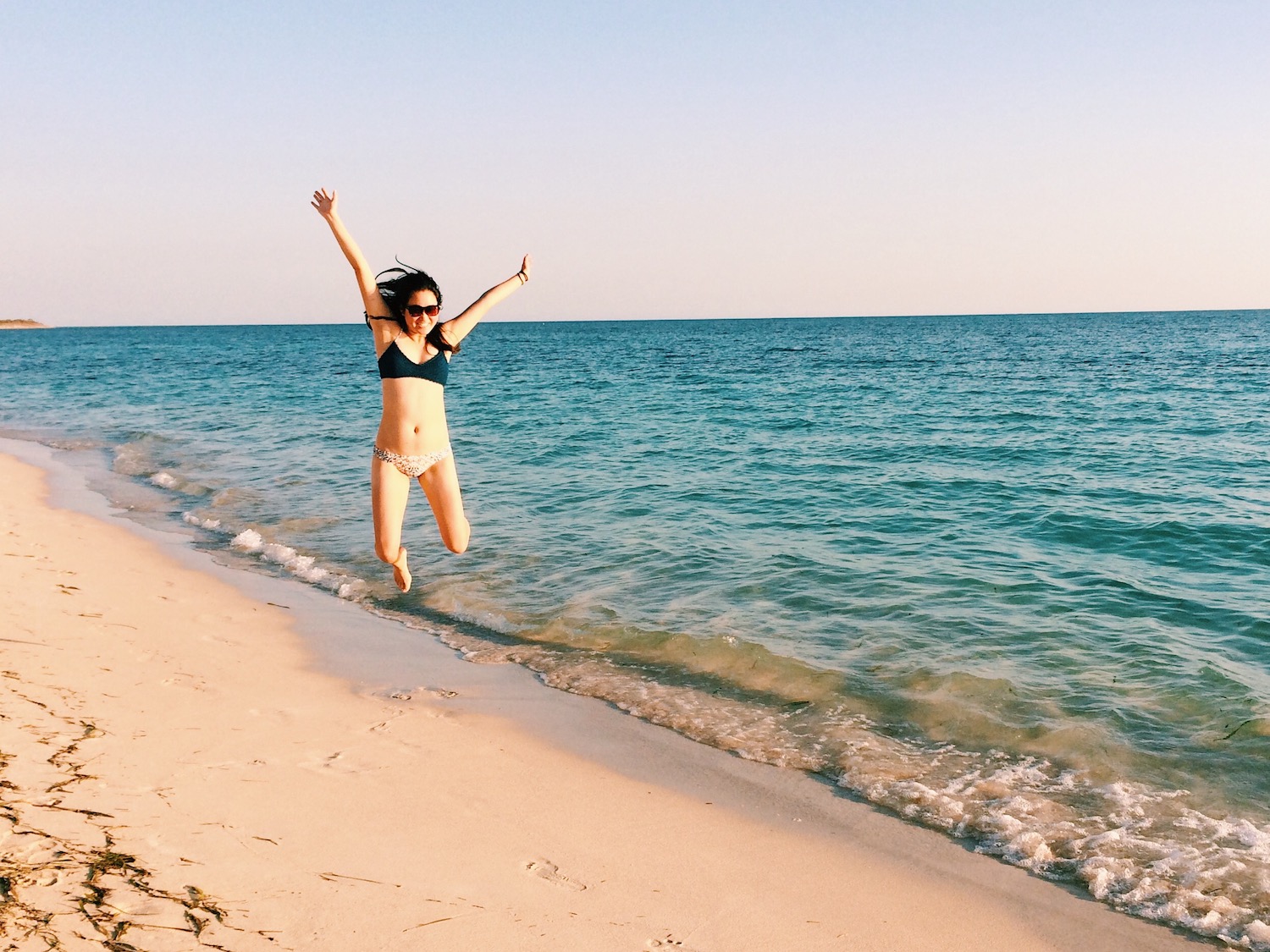 Jumping on the shores of Playa Ancon; also pictured are taupe sand lit from the sunset with turquoise waters rolling in under clear skies