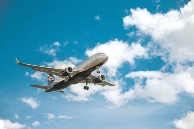 airplane flying in blue skies with slight clouds