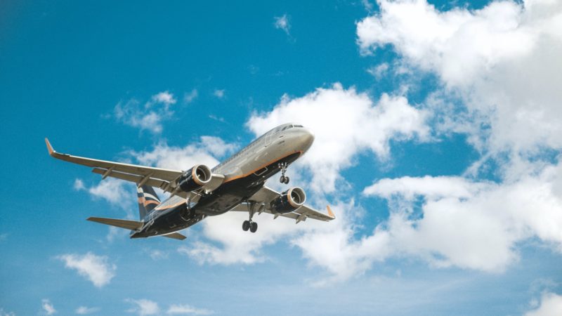 airplane flying in blue skies with slight clouds