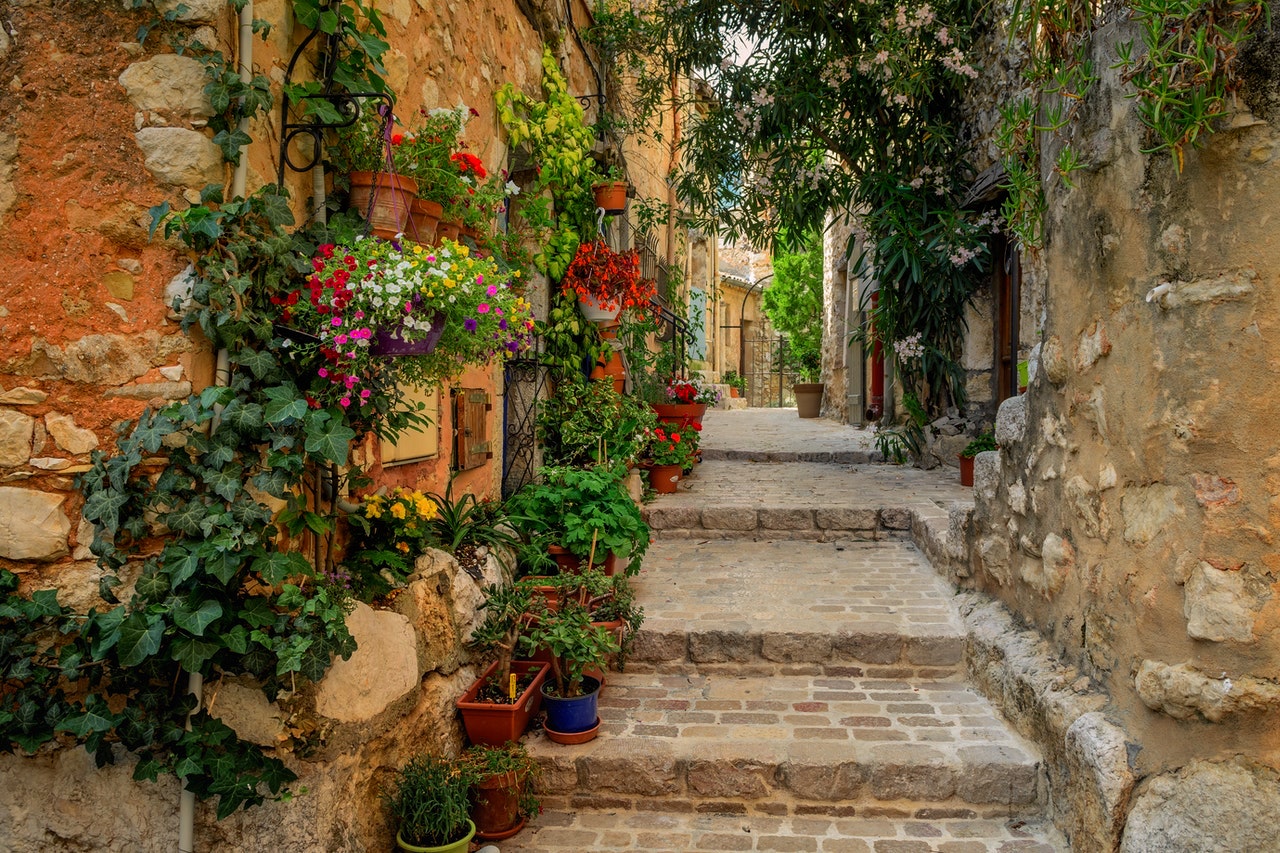 cobblestone steps lined on the left with potted plants and flowers next to an orange painted building