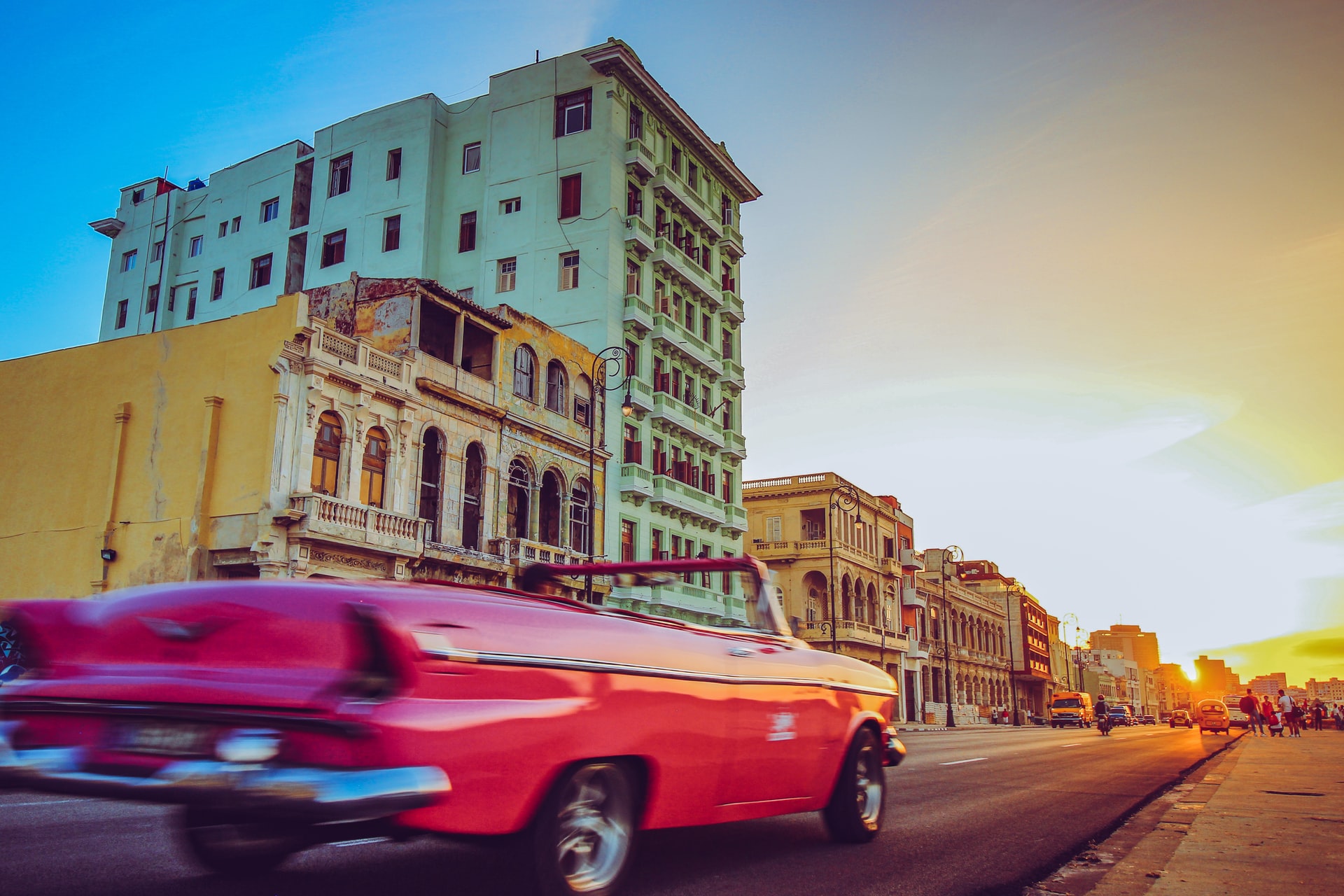 pink convertible driving into sunset past colorful buildings in Havana Cuba