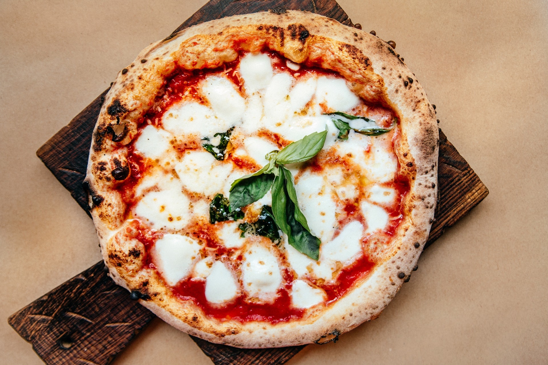 small neapolitan pizza with tomato sauce, cheese, and basil on a brown board