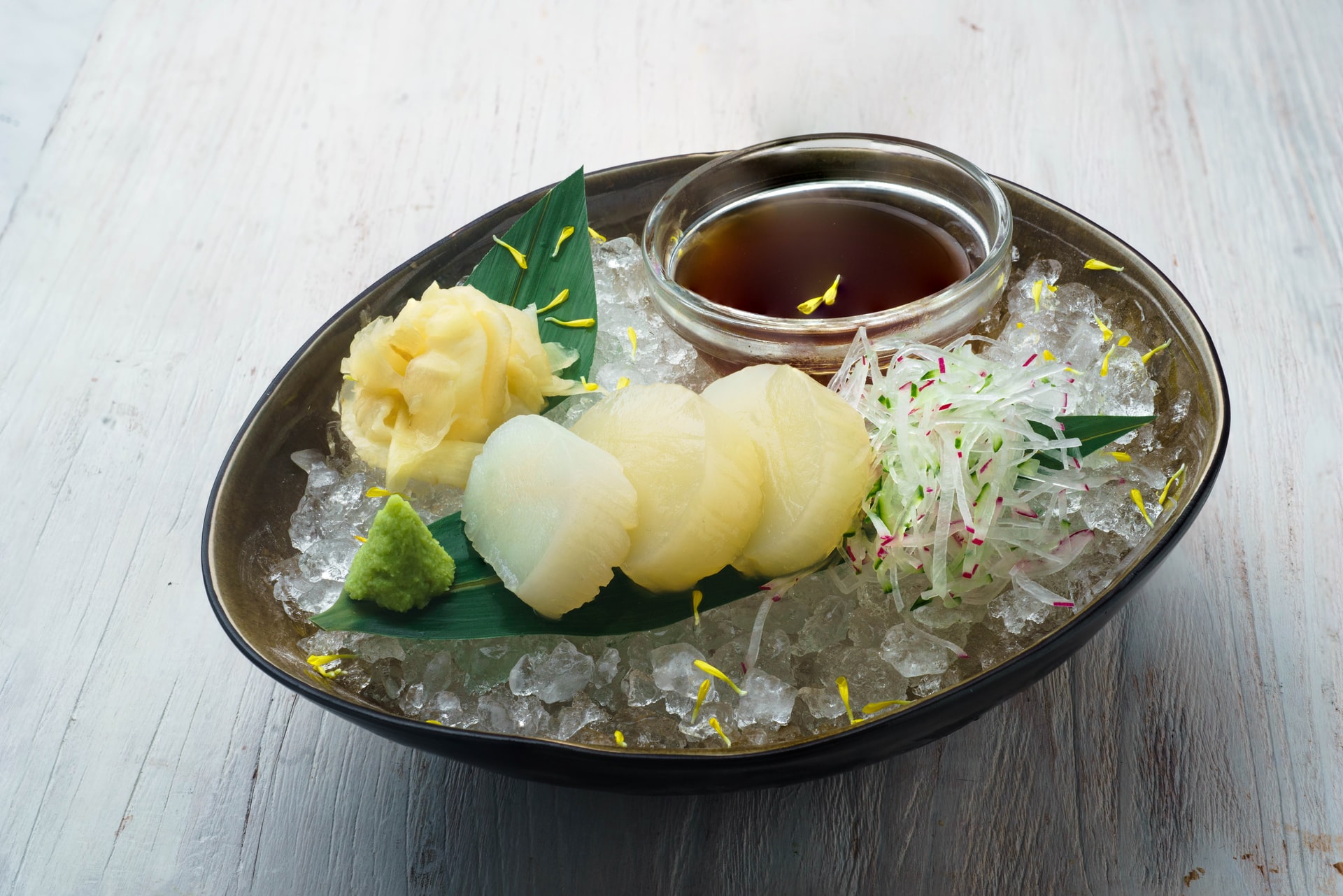 3 slices of scallops on leaf garnish on top of ice with wasabi and soy sauce