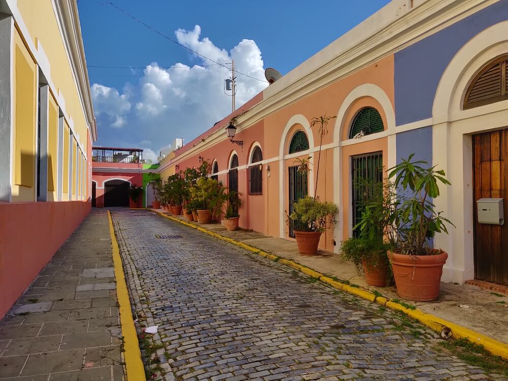colorful buildings in a small cobblestone street lined with potted plants