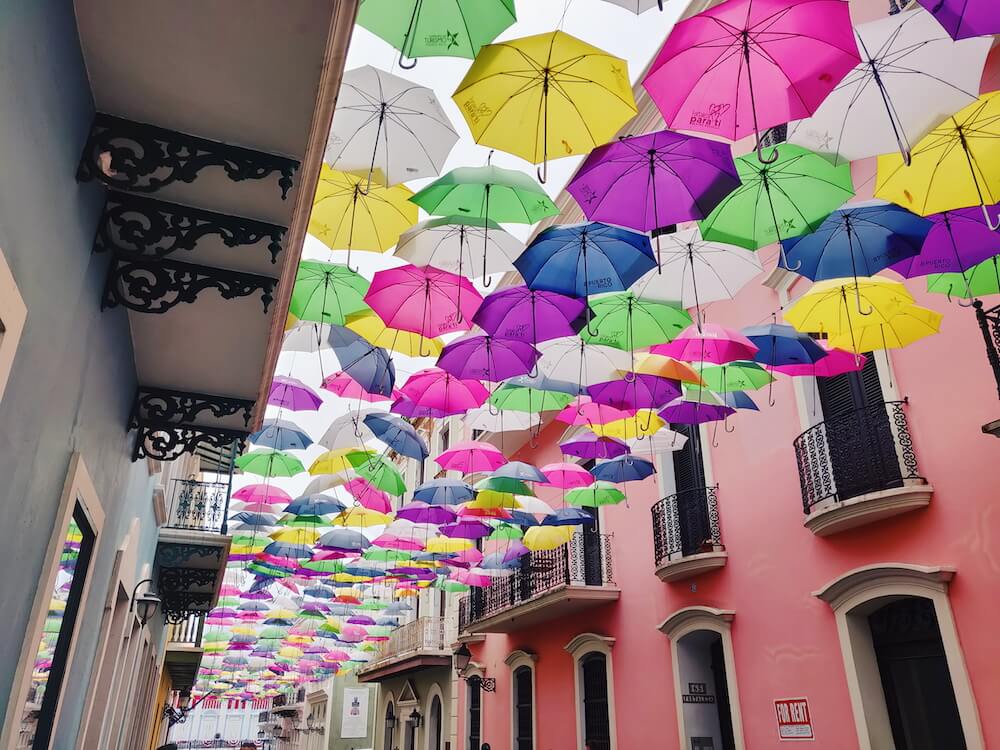 Famous Instagram street in Old San Juan known as Umbrella Street or Calle de Fortaleza; colorful umbrellas hang over the street outside brightly painted buildings