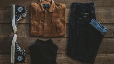 flatlay of tan button-down shirt, black converse sneakers, and dark blue denim jeans