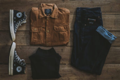 flatlay of tan button-down shirt, black converse sneakers, and dark blue denim jeans
