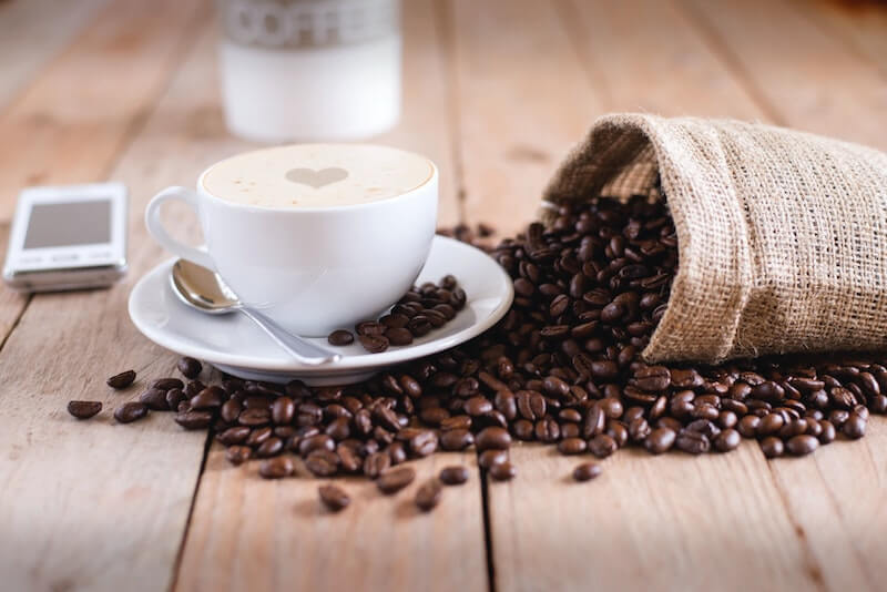 cup of coffee next to bag of spilled coffee beans