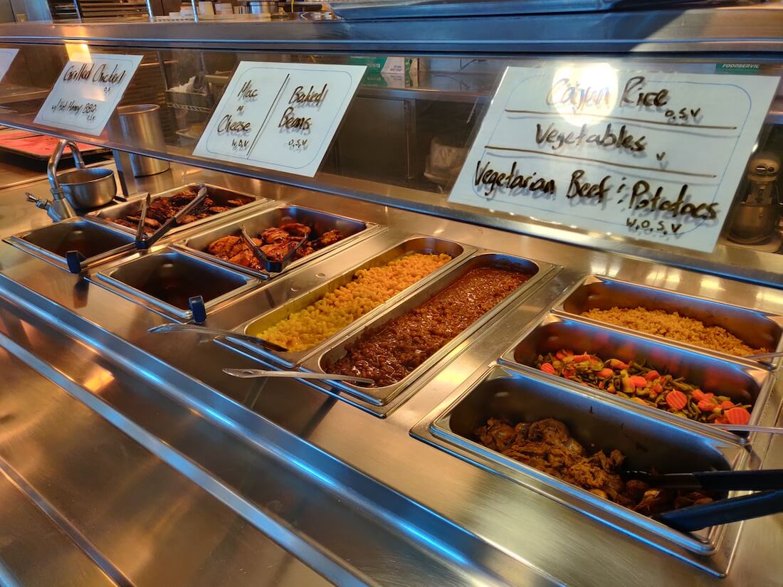 The hot line for a meal at the South Pole. The photo includes item names with allergens and the following food items: grilled chicken, mac & cheese, baked beans, cajun rice, vegetables, vegetarian beef & potatoes