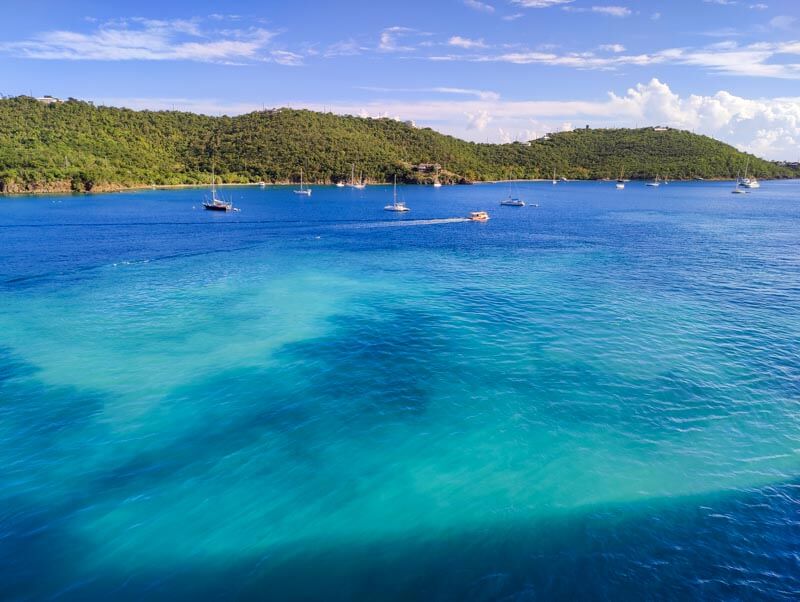 Turquoise blue waters with some boats in front of a lush green mountain
