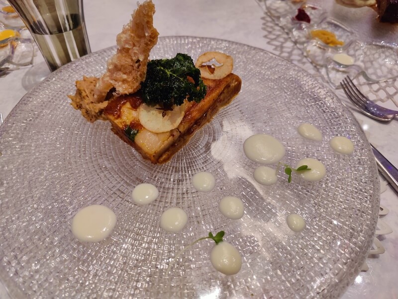 a crispy piece of pork sits on a crystal platter next to decorative dollops of sauce
