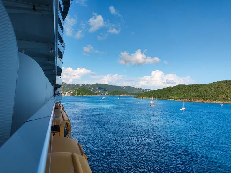 View from cruise ship stateroom balcony with lush green mountains in the distance and small boats in the foreground