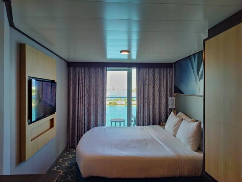 queen bed, flat screen tv, and curtains drawn slightly back to show balcony ocean view