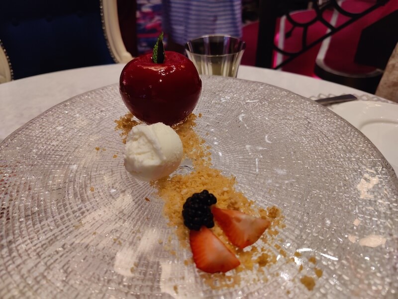 A glazed apple that's really cake inside sits on a crystal platter alongside brown butter crumble, a scoop of white yogurt ice cream, and some berries