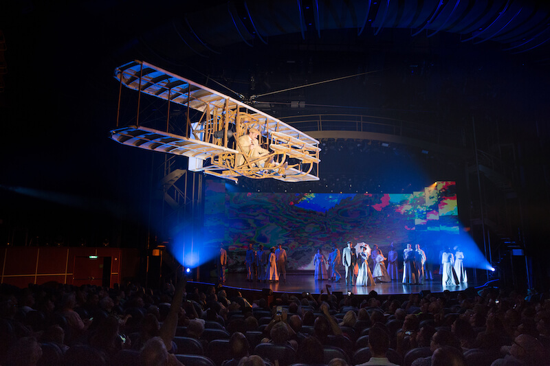 A replica of the Wright brothers' first plane soars above the audience in Symphony of the Seas' "Flight"
