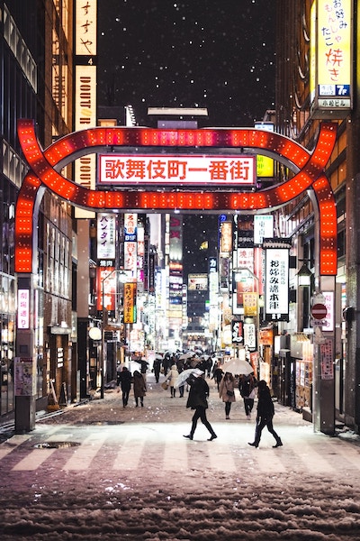 dusting of snow in tokyo's shinjuku neighborhood at night. A street lit up by neon signs has light snowfall while people walk with umbrellas