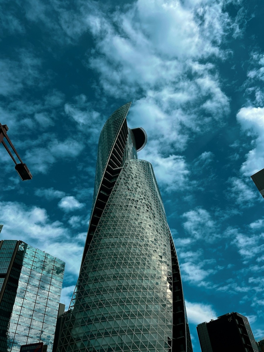 A spiral tower building is photographed from below with dramatic clouds in the background