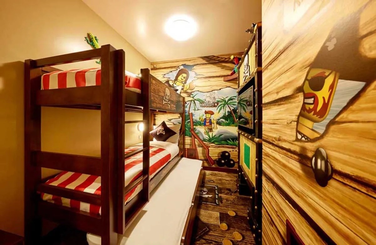 A colorful kids' themed bedroom featuring a bunk bed with red and white striped bedding, pirate-themed murals on the walls, and playful decor elements.